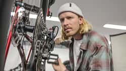 Ein Mann prüft das Schaltwerk und die Kassette eines Fahrrads in einer Werkstattumgebung.