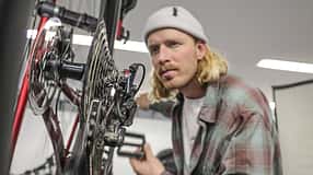 Ein Mann prüft das Schaltwerk und die Kassette eines Fahrrads in einer Werkstattumgebung.