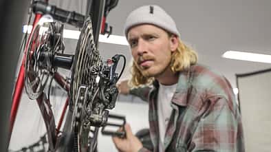 Ein Mann prüft das Schaltwerk und die Kassette eines Fahrrads in einer Werkstattumgebung.