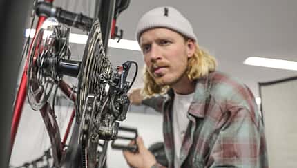 Ein Mann prüft das Schaltwerk und die Kassette eines Fahrrads in einer Werkstattumgebung.