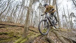 Mountainbiker fährt mit E-Mountainbike einen wurzeligen Trail im herbstlichen Wald bei Stuttgart hinab.