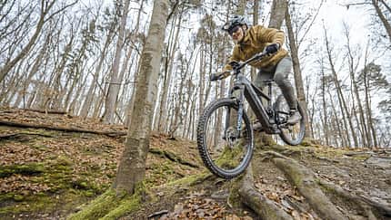 Mountainbiker fährt mit E-Mountainbike einen wurzeligen Trail im herbstlichen Wald bei Stuttgart hinab.
