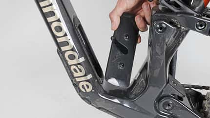Cannondale, Fahrradrahmen, Unterrohr, Abdeckung, Mountainbike, E-Bike, Rahmenfach, Carbonrahmen, Werkzeugfach, Detailaufnahme Detailaufnahme eines Cannondale-Fahrradrahmens mit entnehmbarer Abdeckung im Unterrohrbereich. Eine Hand hält die Abdeckung, die vermutlich Zugang zu einem Fach oder einer Komponente im Rahmen ermöglicht.