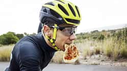 Man eating pizza while cycling on street against clear sky