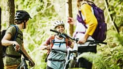 Smiling friends in discussion while resting during mountain bike ride in forest