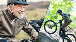 Älteres Paar mit Helmen fährt lachend auf E-Bikes durch eine hügelige Landschaft.