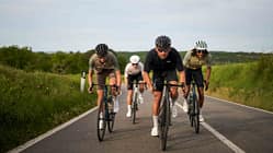 Drei Rennradfahrer fahren in Teamformation auf einer offenen Landstraße, flankiert von grüner Natur.