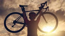 Rear view of cyclist woman lifting her bicycle above her head after finished her exercise workout during sunset.