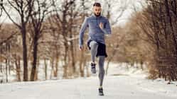 Junger Sportler läuft im Wald auf einem schneebedeckten Weg.
