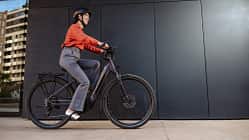 Eine Frau pendelt bequem mit einem Elektrofahrrad, gekleidet in Freizeitkleidung mit Sicherheitsausrüstung.  Eine Frau pendelt bequem mit einem Elektrofahrrad, gekleidet in Freizeitkleidung mit Sicherheitsausrüstung.