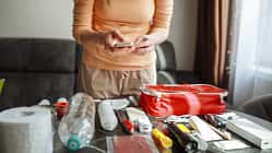 Frau überprüft mit ihrem Smartphone den Inhalt eines Notfallkits, Krisenvorsorge zu Hause