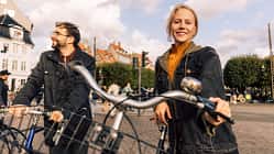 Porträt einer lächelnden Frau, die neben einem männlichen Freund mit Fahrrad auf einer Straße in der Stadt steht.