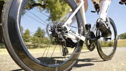 Die Aufnahme zeigt das Rennrad Look 795 Blade RS aus der Perspektive des Hinterrades während der Fahrt. Sichtbar sind der Carbonrahmen, eine Kassette mit Schaltwerk, tiefprofilige Aero-Laufräder sowie eine Scheibenbremse am Hinterrad. Der Fokus liegt auf dem Antrieb und der Bremsanlage auf einer sonnigen Straße im Freien.