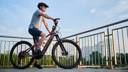 Mann fährt E-Bike auf der Stadtpromenade, Seitenansicht Radfahrer gegen blauen Himmel. 