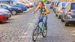 Olaf Schubert fährt ein Retro-Fahrrad auf einem Parkplatz