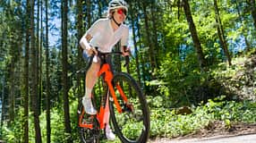 Frontalansicht einer Radsportlerin auf dem orangenen Storck Fascenario.5 in Fahrt auf einer Landstraße im Wald.