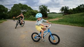 Portrait of excited little boy with his family at backround riding bike on path in park in summer Portrait of excited little boy with his family at backround riding bike on path in park in summer