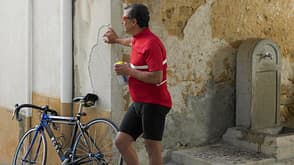 Easy Retouch,Colour Image,Photography,vertical,outdoors,day,full length,leaning,standing,60-65 years,one senior man only,adults only,only men,one person,urban scene,building exterior,old town,bicycle,pavement,leisure,recreational pursuit,sport,sports clothing,taking a break,contemplation,Caucasian Appearance,racing bicycle,refreshment,water bottle Cyclist leaning on wall of building in old town