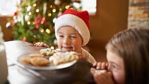 Weihnachtsmarkt, Ernährun, Zuckerwatte, Maronen, Plätzchen Kinder betrachten über die Tischkante hinweg einen Teller Plätzchen