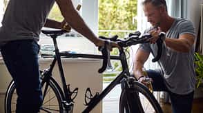 Two casual mature men examining bicycle at home