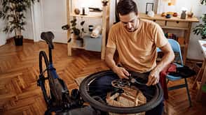 Young casually clothed man inflating bicycle tire in his apartment
