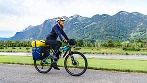 rock Woman cyclist rides bicycle using bike lane along river and mountains.