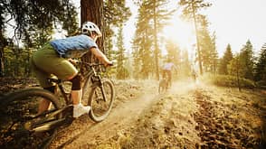 Female mountain bikers descending down forest trail together on summer evening Female mountain bikers descending down forest trail together on summer evening