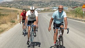 Easy Retouch,Colour Image,Photography,horizontal,outdoors,day,front view,full length,smiling,60-65 years,senior men,adults only,only men,three people,active,healthy lifestyle,young at heart,retirement,active seniors,non-urban scene,transportation,road,bicycle,horizon over land,landscape,hills,leisure,recreational pursuit,sport,sports clothing,motion,action,cycling,on the move,contented,enjoyment,togetherness,Caucasian Appearance,cyclist,racing bicycle Three senior cyclists on country road