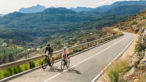 coll de rates Front elevated/drone view of a mature man and his teenage daughter riding their road bikes (race bike) up a climb in the Spanish mountains