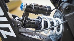 Detailaufnahme eines vollgefederten Mountainbike-Dämpfers mit Federbein und Ausgleichsbehälter, nass vom Wasser.