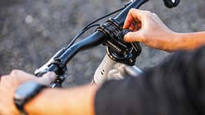 Detailaufnahme eines Fahrradlenkers mit Vorbau, an dem eine Person eine Einstellschraube bedient.