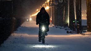 Dunkel gekleideter Radfahrer auf verschneiter Fahrbahn. 