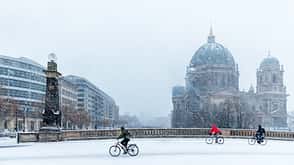 Berliner Dom im Schnee, drei Radfahrer auf der Straße. 
