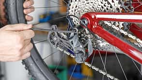 Detailaufnahme eines Fahrradhinterrads mit Kettenschaltung, bei der eine Person das Schaltwerk justiert.