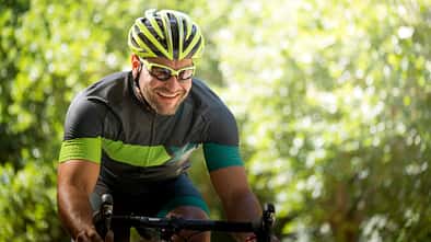 Smiling young man riding bicycle against trees