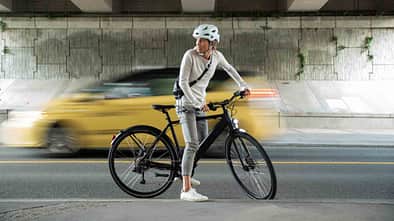A woman riding a battery-powered commuter e-bike through Vancouver, passing iconic locations like Gastown and Stanley Park, with a view of the downtown city skyline.