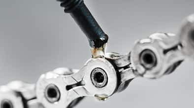Greasing a bicycle chain with a drop of golden oil close-up on a gray background