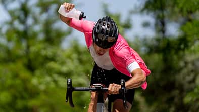 Athlete riding bicycle pouring water from bottle on sunny day