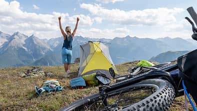 Woman bikepacking and camping, she set up her tent on top of the mountains, arms up Woman bikepacking and camping, she set up her tent on top of the mountains, arms up