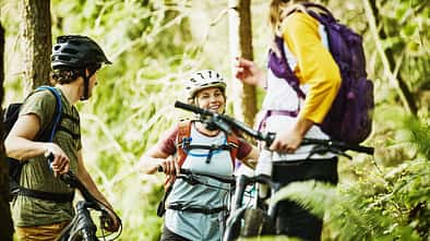 Smiling friends in discussion while resting during mountain bike ride in forest