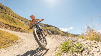 Mountainbiker fährt dynamisch auf Schotterweg durch sonnige Hügellandschaft