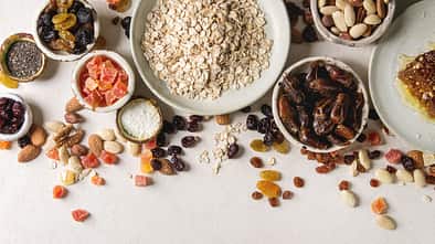 Variety of dried fruits. nuts. honey and oat flakes in ceramic bowls for cooking homemade healthy breakfast muesli or granola energy bars over white texture background. Flat lay. space.