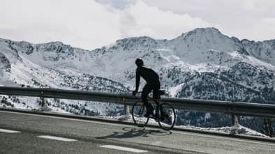 Andorra, cyclist on mountain road with snowy mountains in the background
