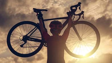 Rear view of cyclist woman lifting her bicycle above her head after finished her exercise workout during sunset.