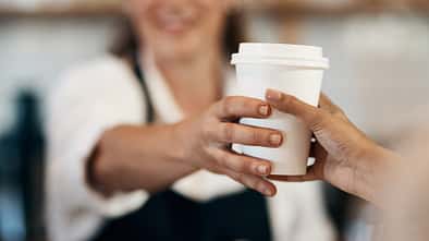 Beschnittene Aufnahme eines Baristas, der einem Kunden in einem Café einen Becher Kaffee reicht