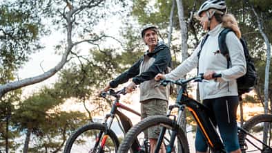 Aktives Seniorenpaar mit Fahrrädern bei Sonnenaufgang am Meer.