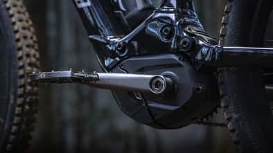 Detailaufnahme eines E-Bike-Mittelmotors mit Kurbel und Pedal, montiert an einem Mountainbike-Rahmen.