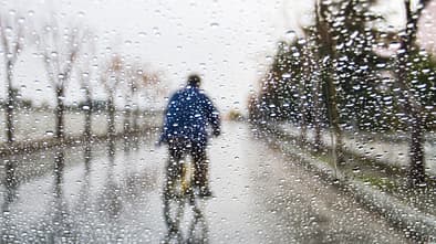 Durch Regentropfen verschwommenes Bild eines Radfahrers mit blauem Regencape. 