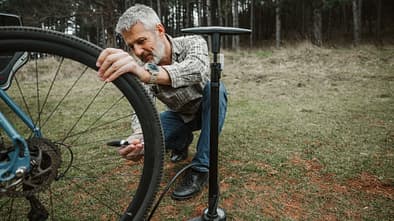Ein Mann pumpt einen Reifen mit einer Standpumpe auf einer Wiese auf. 