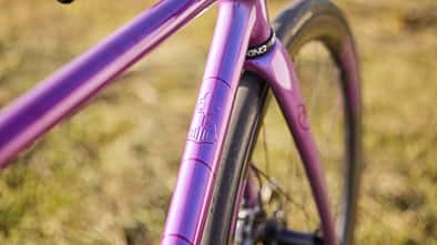 Detailaufnahme des lilafarbenen Fahrradrahmens eines IRIS x St Joris Modells, Fokus auf Steuerrohr und Branding.